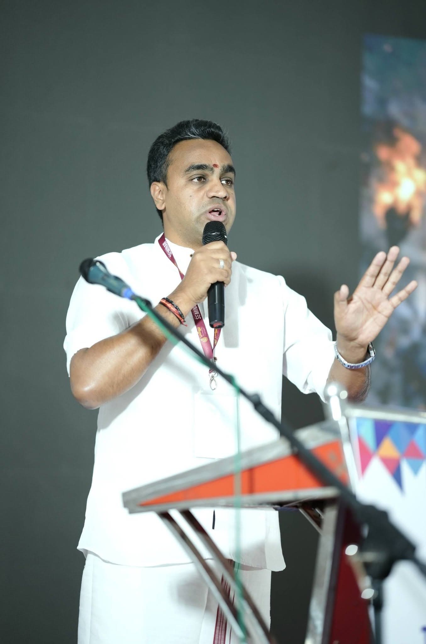 Manesh speaking at a lectern with one hand raised